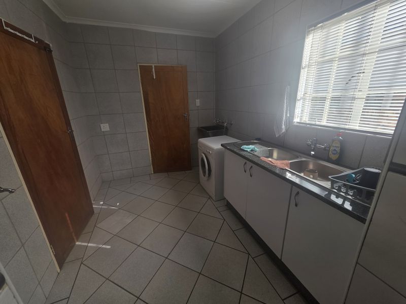 A functional laundry room featuring tiled walls and floors, a double basin sink with laminate countertop, and built-in cabinetry for storage.