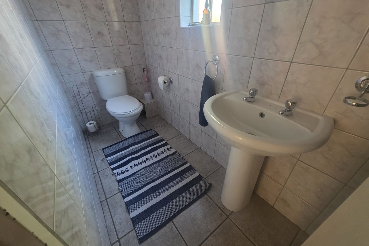 A functional bathroom featuring a pedestal basin, toilet, and full-height wall tiling.