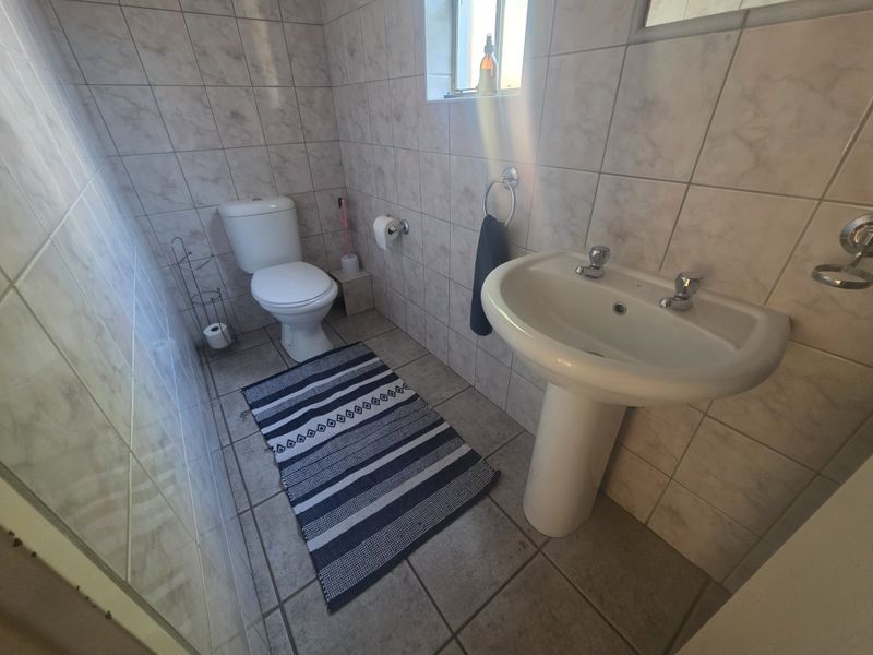 A functional bathroom featuring a pedestal basin, toilet, and full-height wall tiling.