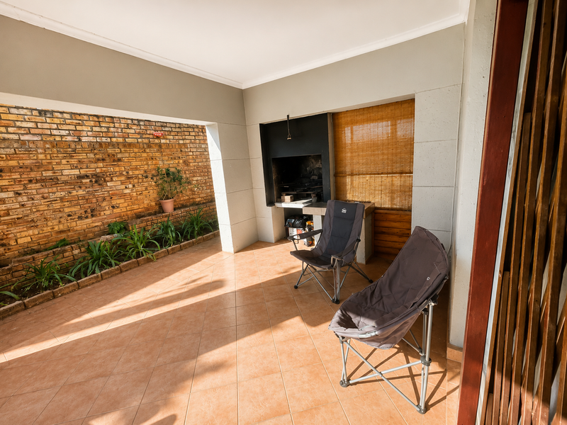 Covered patio area featuring a built-in braai, exposed brick wall, and tiled flooring, providing a functional outdoor entertainment space.