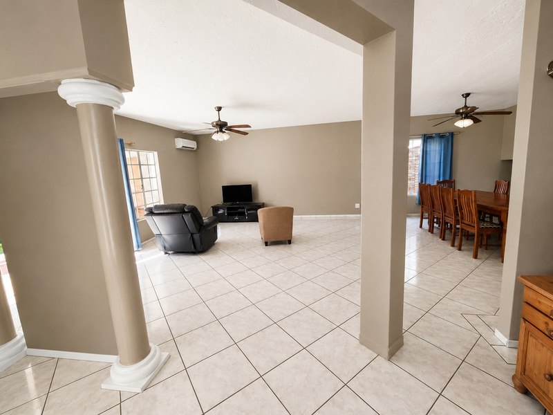 Spacious open-plan living and dining area featuring ceramic tile flooring, decorative columns, and dual ceiling fans for climate control.