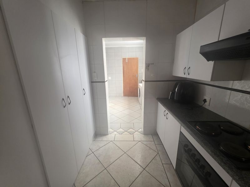 A functional scullery area featuring white built-in cabinetry, tiled finishes, and integrated cooking appliances, leading through to an adjacent utility space.