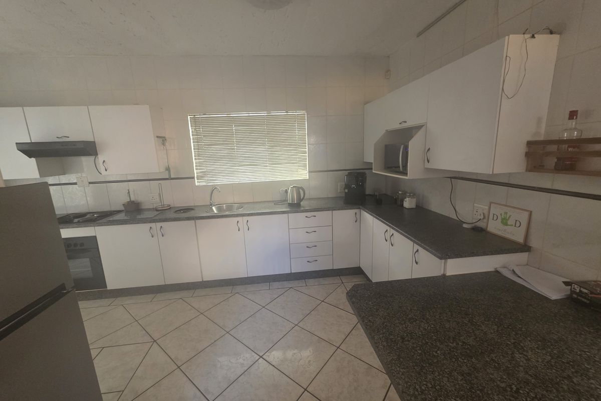 A functional kitchen featuring white cabinetry, dark countertops, tiled flooring, and integrated appliances, offering a practical layout with potential for modern updates.