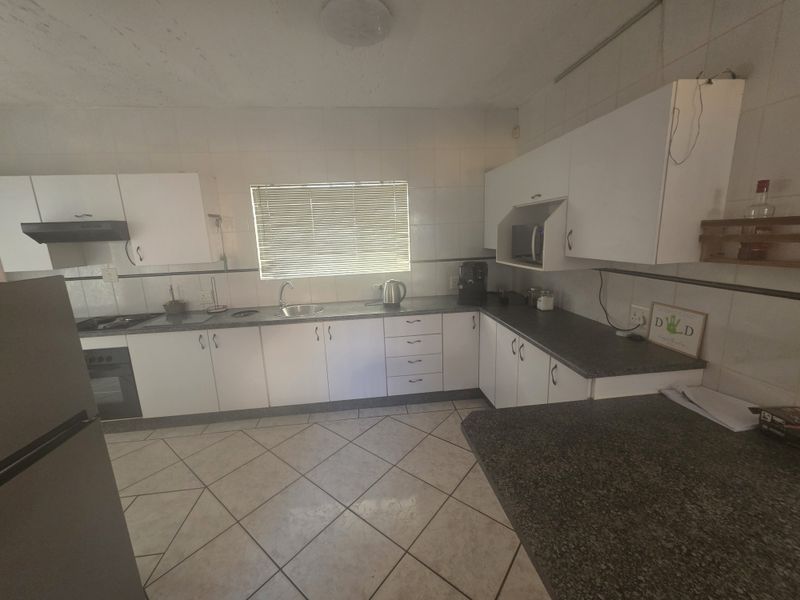 A functional kitchen featuring white cabinetry, dark countertops, tiled flooring, and integrated appliances, offering a practical layout with potential for modern updates.