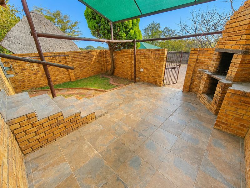Outdoor patio area featuring a built-in brick braai, tiled flooring, and a shade cloth structure, perfect for entertaining.