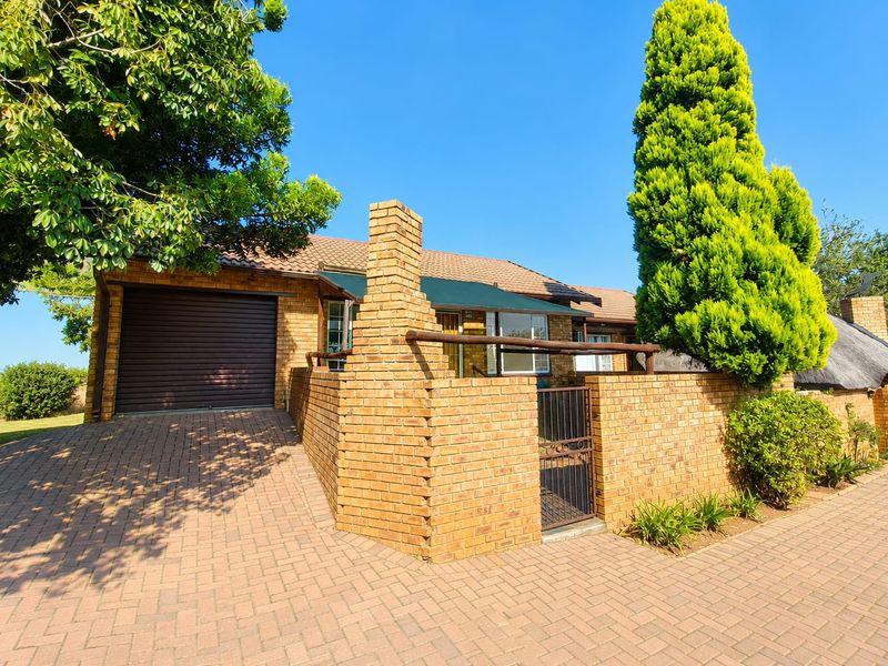 Front exterior view of a brick townhouse featuring a paved driveway, single garage, and a private walled entrance area.