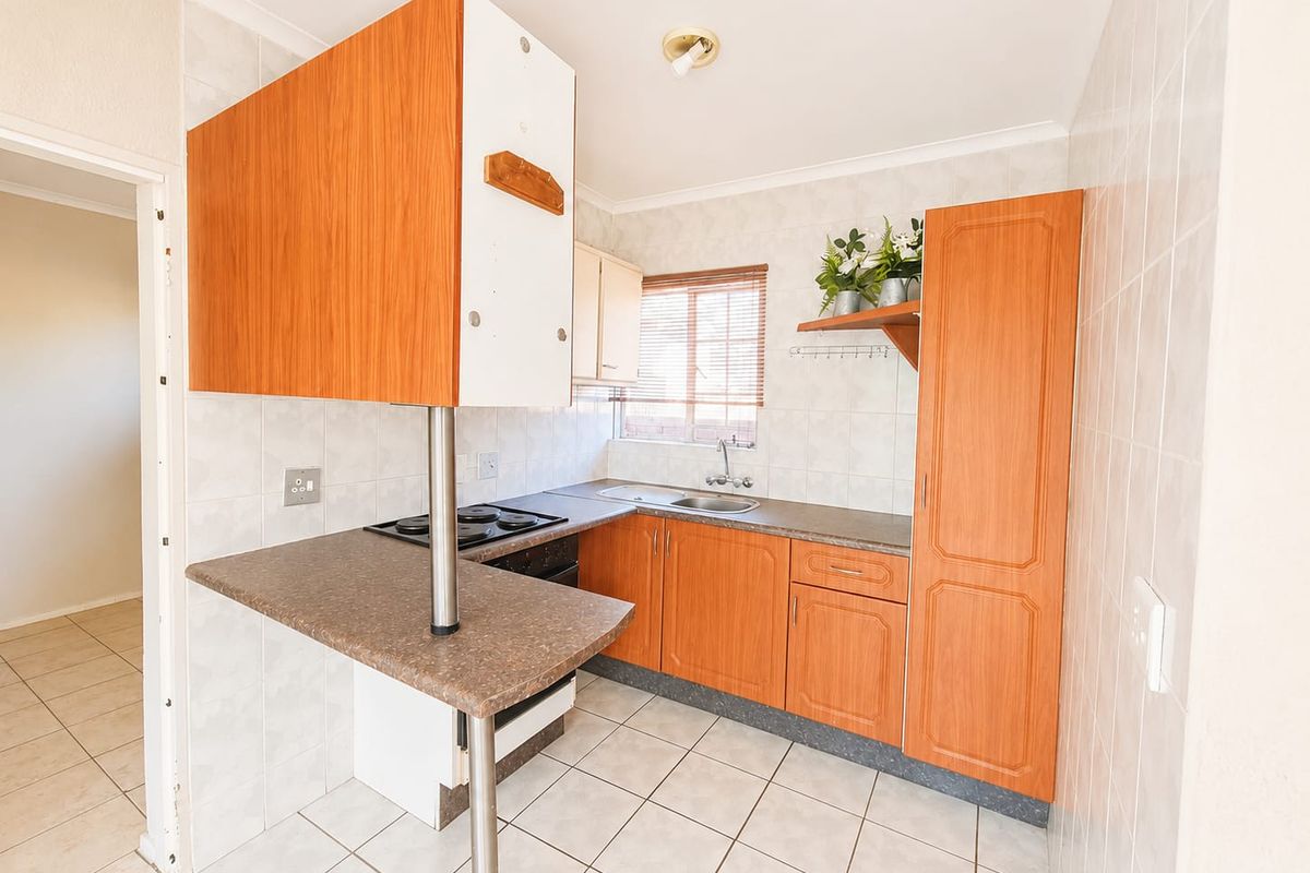 A functional kitchen featuring laminate cabinetry, built-in oven and hob, tiled flooring, and a breakfast counter, offering a practical layout for daily use.