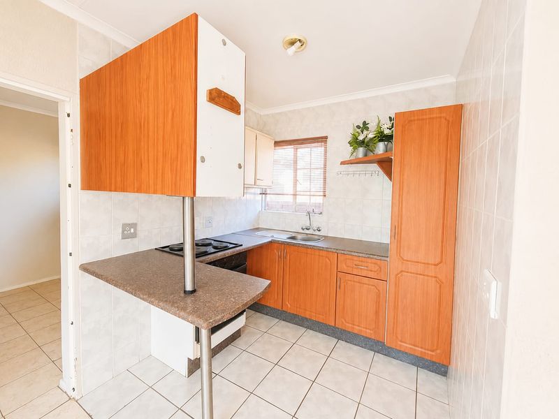 A functional kitchen featuring laminate cabinetry, built-in oven and hob, tiled flooring, and a breakfast counter, offering a practical layout for daily use.