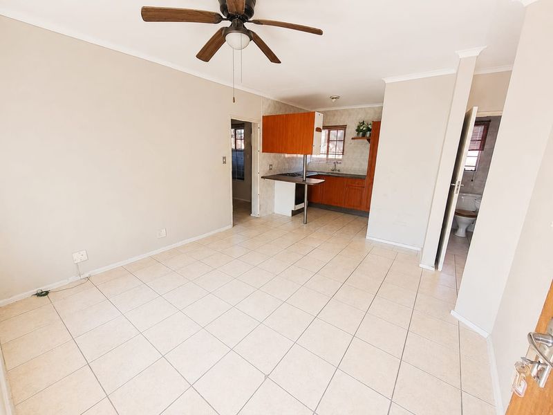 Open plan living area featuring tiled flooring, a ceiling fan, and an adjoining kitchen with built-in cabinetry and stove.