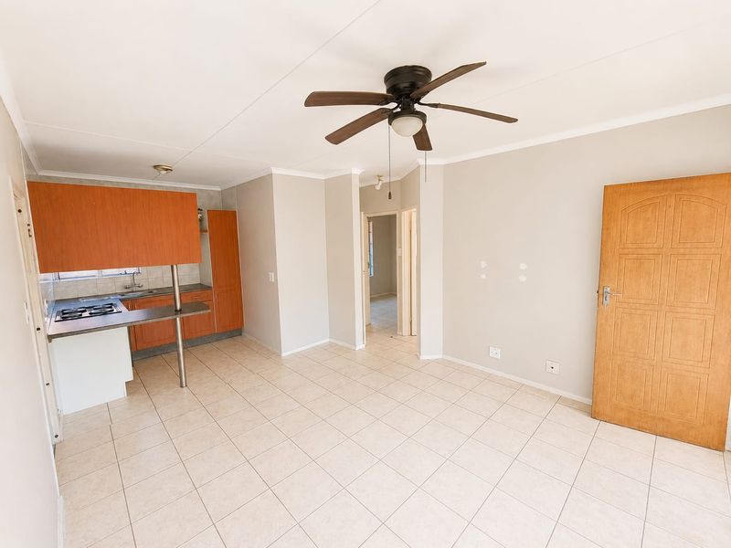 An open-plan living and kitchen area featuring tiled flooring, a ceiling fan, and functional built-in cabinetry with a breakfast counter.