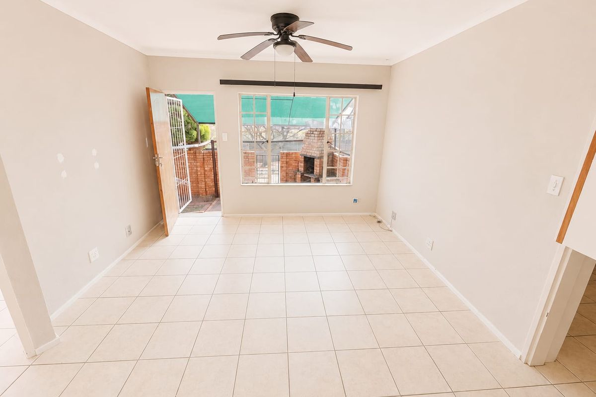 An empty, light-filled living room featuring tiled flooring, a ceiling fan, and direct access to an outdoor patio area.