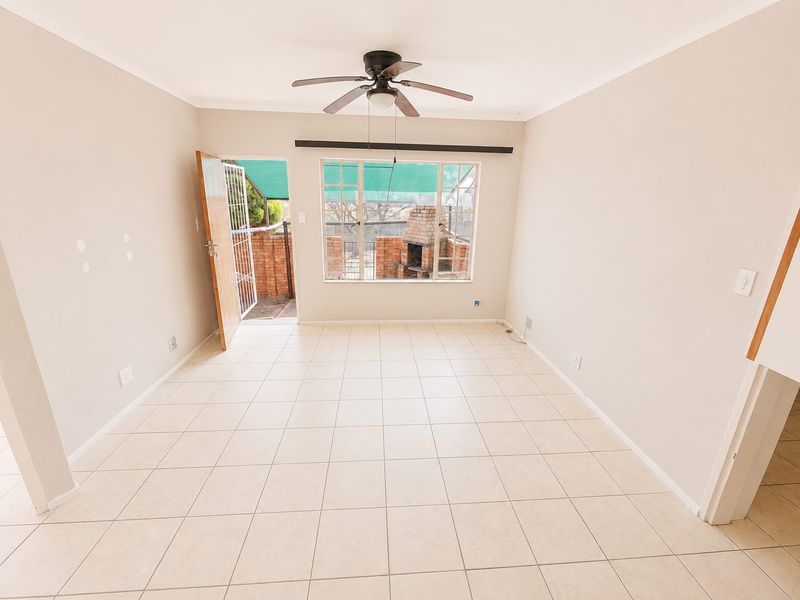 An empty, light-filled living room featuring tiled flooring, a ceiling fan, and direct access to an outdoor patio area.