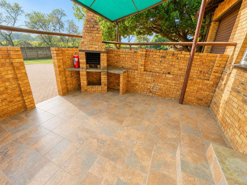 A covered outdoor patio area featuring a built-in brick braai, tiled flooring, and a shade cloth canopy, perfect for outdoor entertaining.