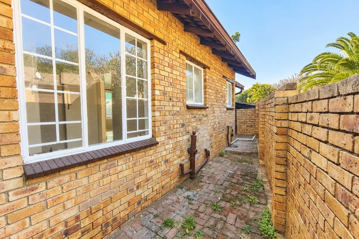 A side exterior view of the townhouse featuring face brick walls, a paved walkway, and a brick boundary wall.