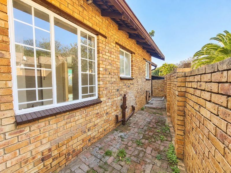 A side exterior view of the townhouse featuring face brick walls, a paved walkway, and a brick boundary wall.