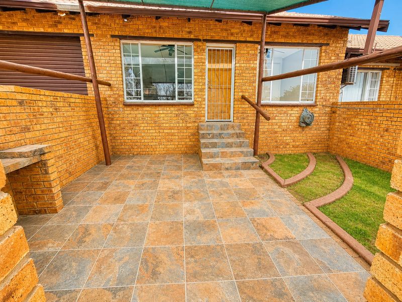 A private paved patio area featuring a built-in brick braai, tiled steps, and a shade cloth awning, enclosed by face-brick boundary walls.