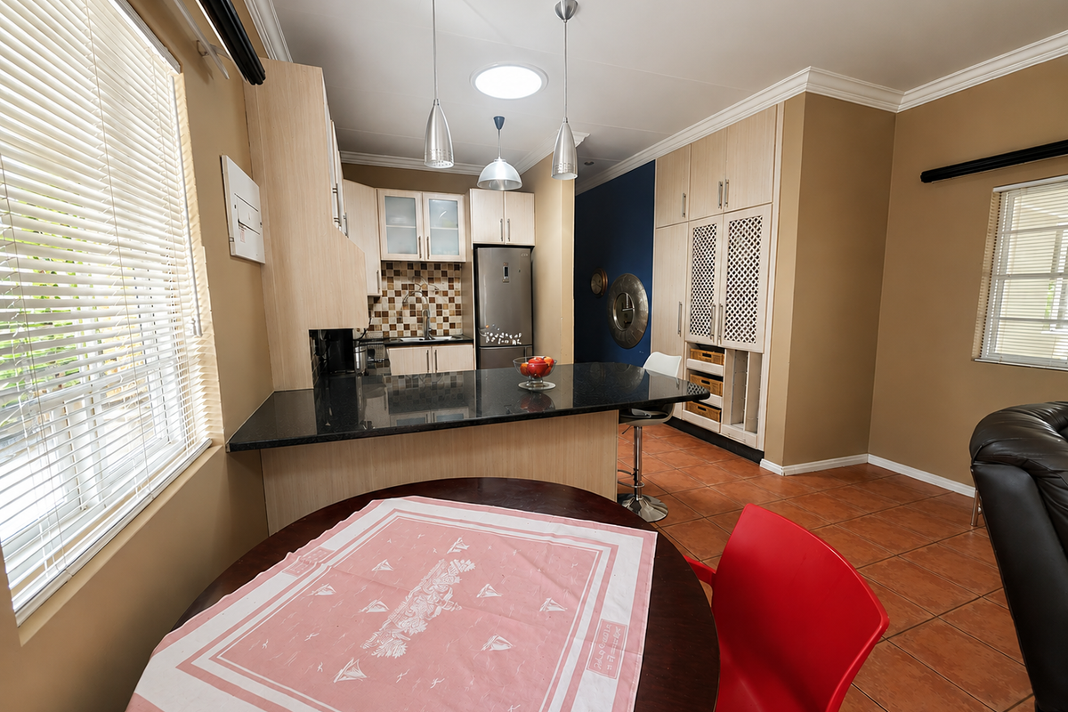 Open-plan kitchen and dining area featuring granite countertops, built-in cabinetry, tiled flooring, and natural light from a skylight and windows.