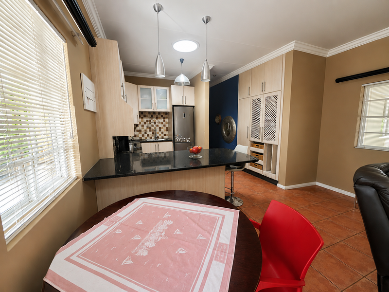 Open-plan kitchen and dining area featuring granite countertops, built-in cabinetry, tiled flooring, and natural light from a skylight and windows.
