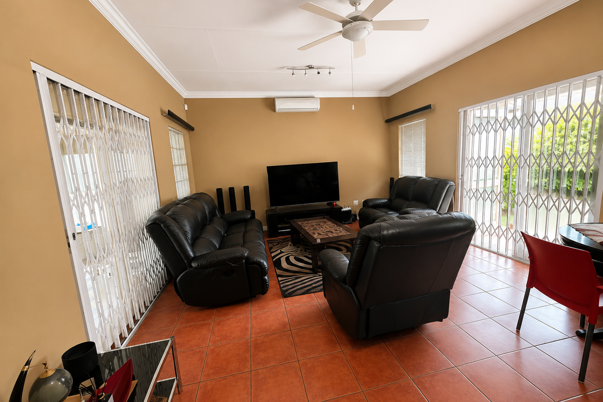 A spacious living room featuring terracotta tiled flooring, a ceiling fan, split-system air conditioning, and security gates leading to outdoor areas.