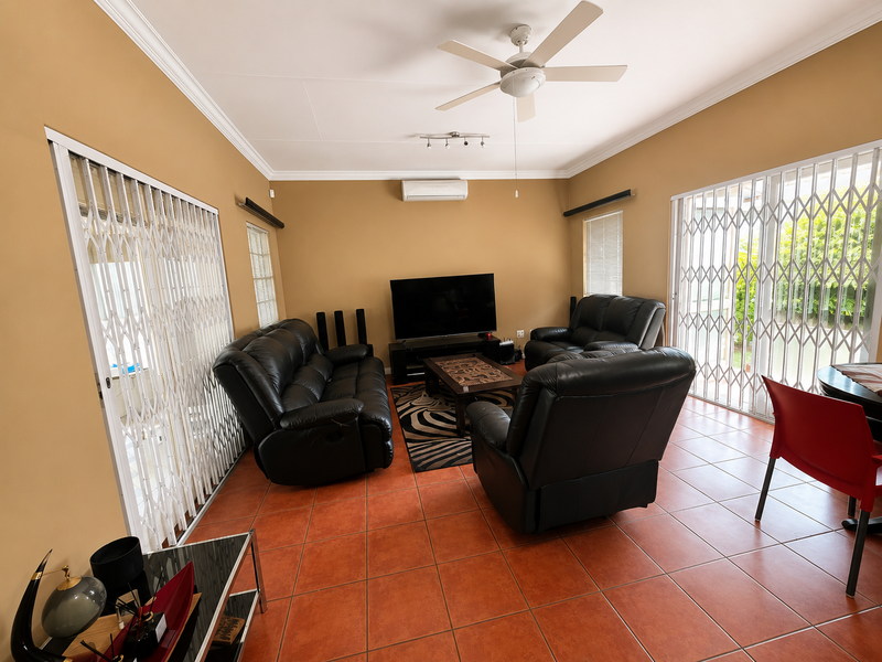 A spacious living room featuring terracotta tiled flooring, a ceiling fan, split-system air conditioning, and security gates leading to outdoor areas.