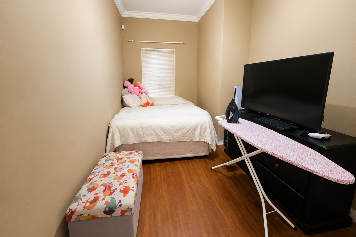 A compact bedroom featuring laminate flooring, crown molding, and a window fitted with venetian blinds.