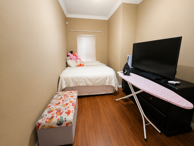 A compact bedroom featuring laminate flooring, crown molding, and a window fitted with venetian blinds.
