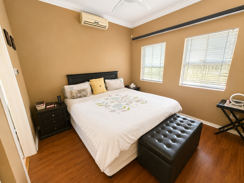 A well-lit bedroom featuring laminate flooring, crown molding, a ceiling fan, and a wall-mounted split-system air conditioner.