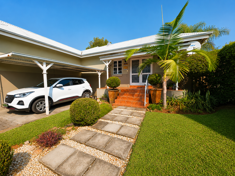 Front exterior view of the townhouse featuring a covered carport, paved walkway, and tiled entrance steps leading to the main door.