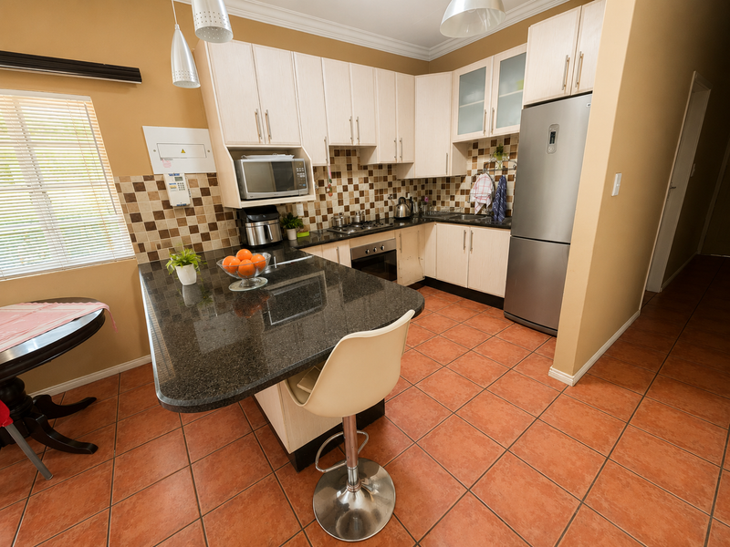 A functional kitchen featuring granite countertops, built-in oven, gas hob, and light-toned cabinetry with a tiled backsplash and ceramic flooring.