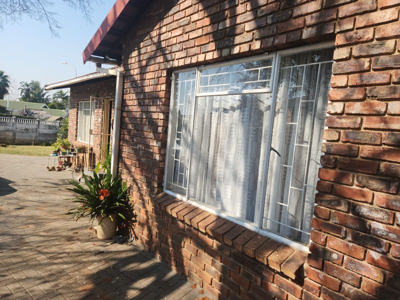 A view of the rear exterior featuring a classic face brick facade, paved patio area, and secure window installations.