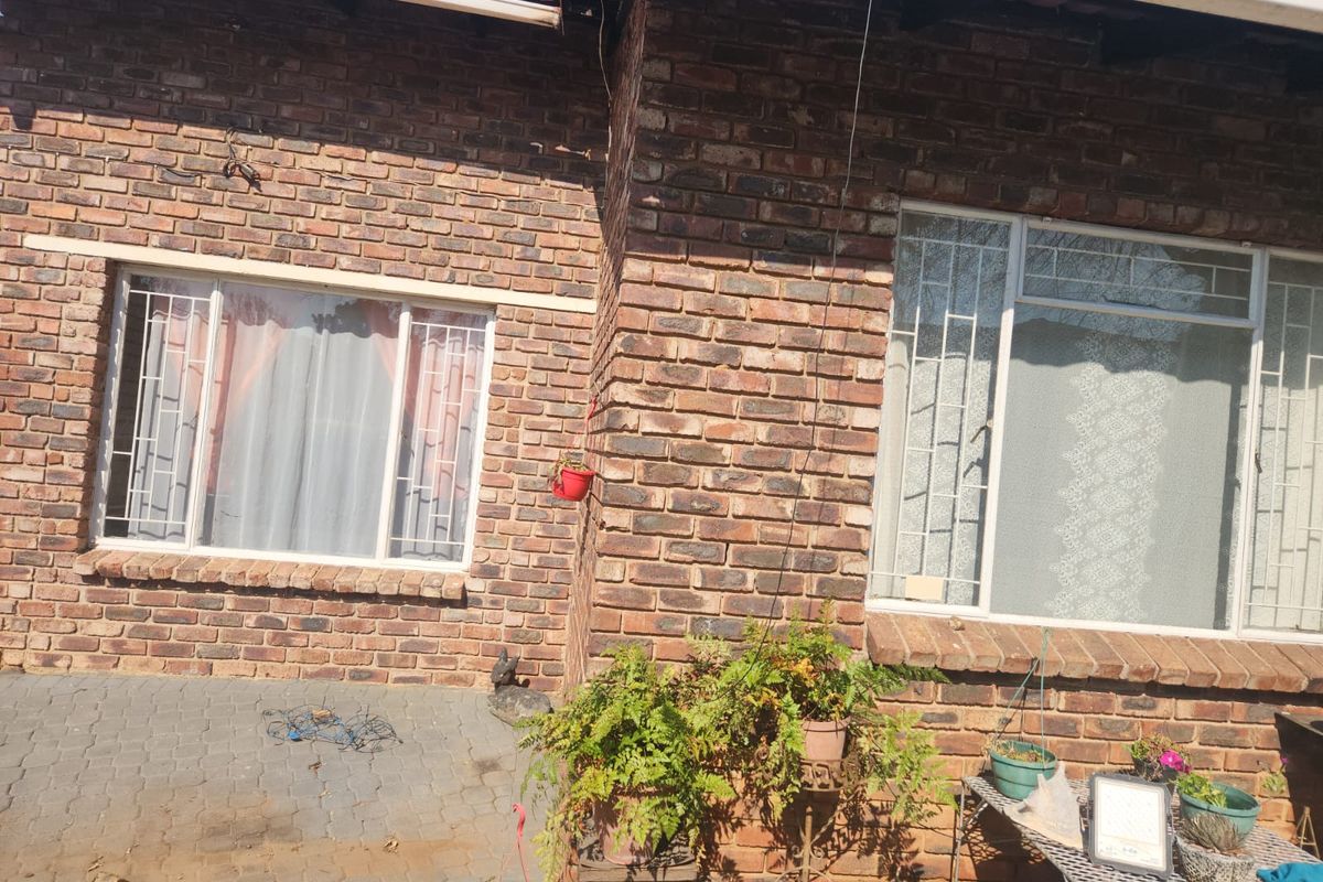 A view of the rear face brick facade featuring security bars on the windows and a paved patio area.