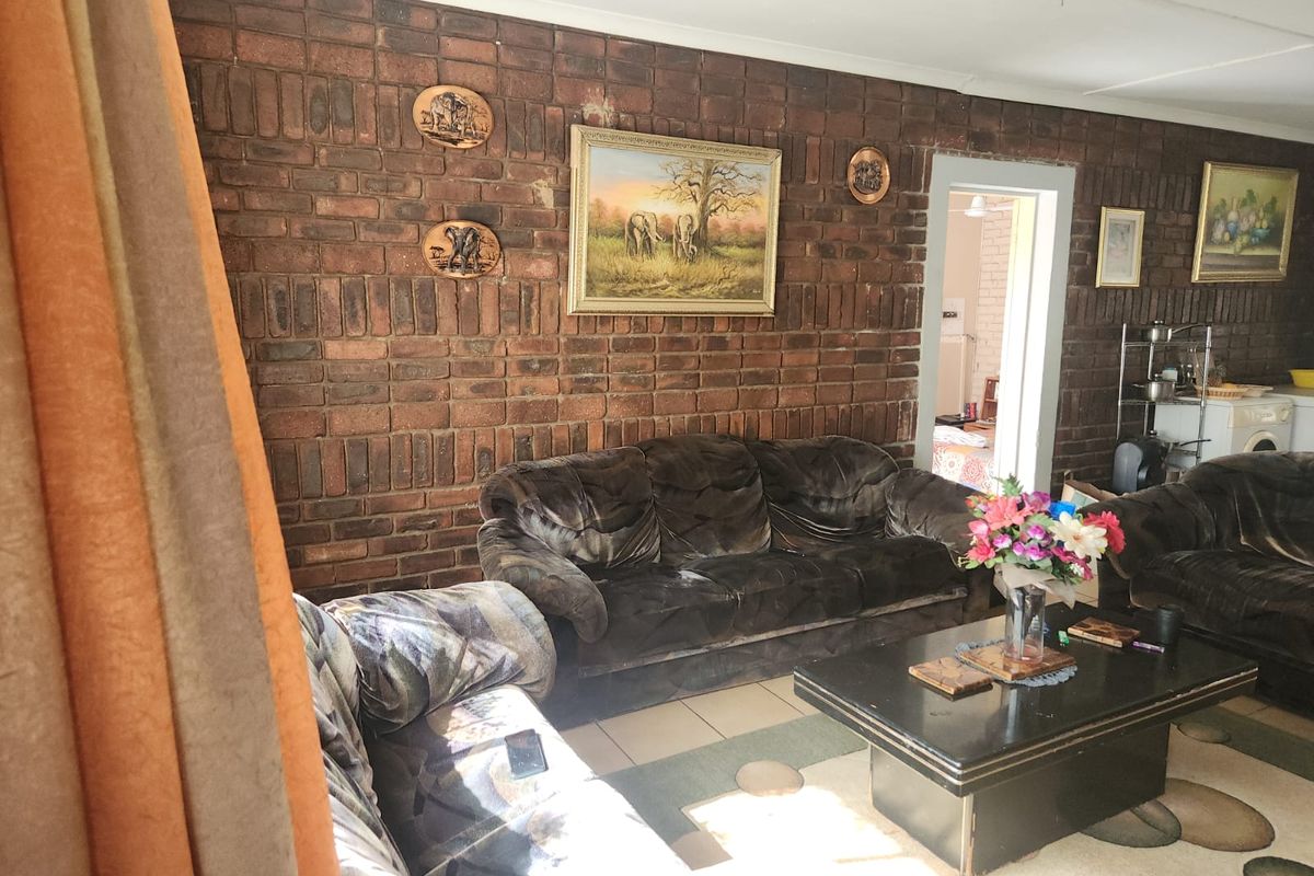 Living room featuring an exposed brick feature wall, tiled flooring, and a ceiling fan, providing a rustic foundation for potential interior updates.