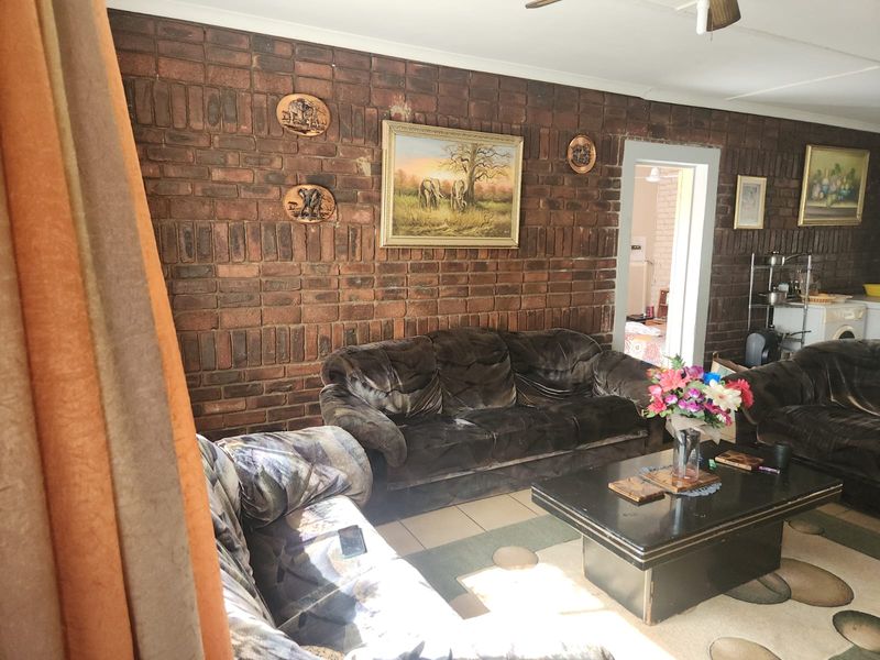 Living room featuring an exposed brick feature wall, tiled flooring, and a ceiling fan, providing a rustic foundation for potential interior updates.