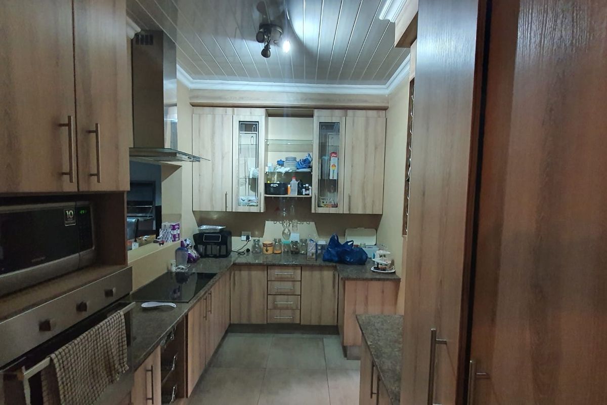 A functional kitchen featuring wood-look cabinetry, integrated appliances including an oven and hob, tiled flooring, and a tongue and groove ceiling.
