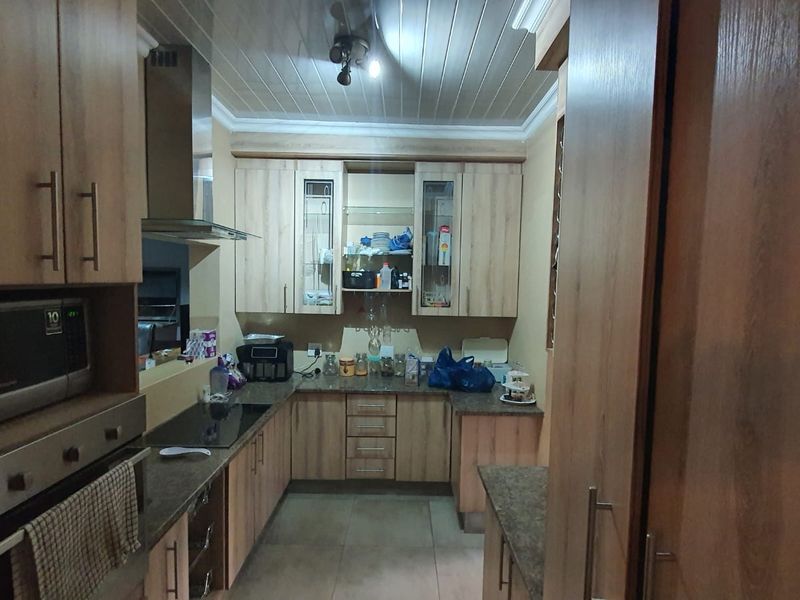 A functional kitchen featuring wood-look cabinetry, integrated appliances including an oven and hob, tiled flooring, and a tongue and groove ceiling.