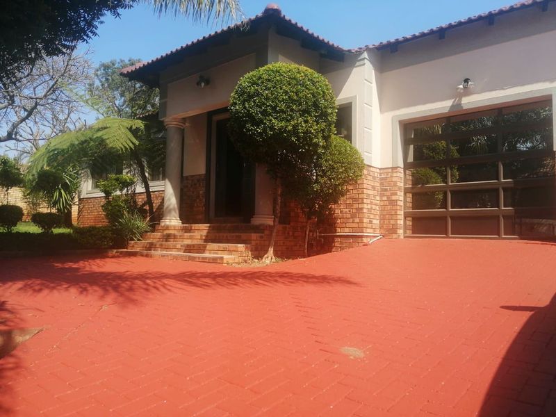 Front elevation of a townhouse featuring a brick facade, covered entrance with columns, and a paved driveway leading to a garage.