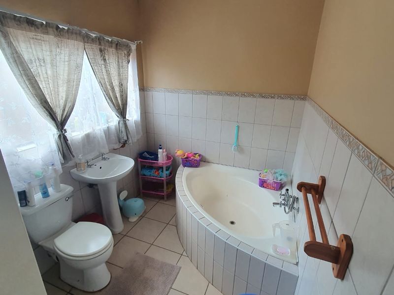 A functional bathroom featuring a corner bathtub, pedestal basin, and toilet with tiled splashbacks and flooring.