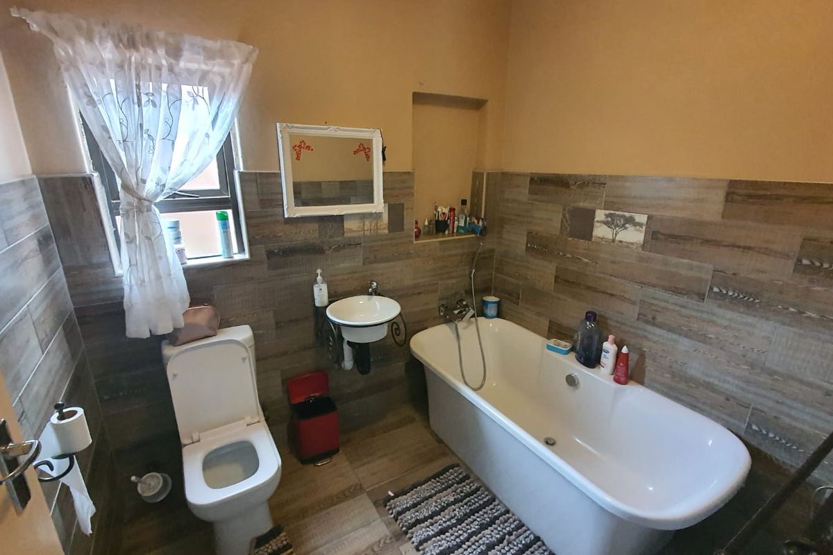 A functional bathroom featuring a bathtub, wall-mounted basin, toilet, and wood-look tiled walls with a convenient recessed storage niche.