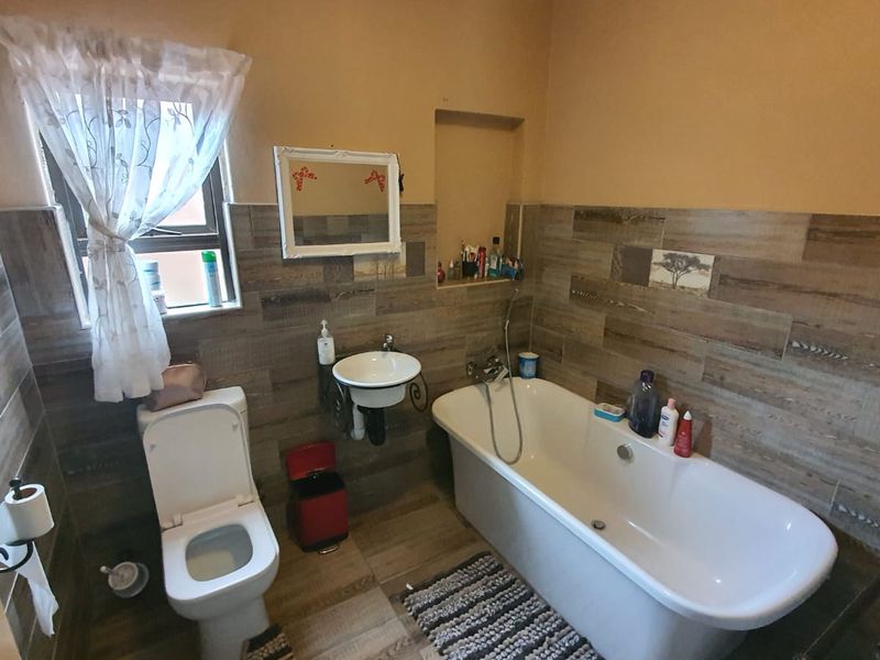 A functional bathroom featuring a bathtub, wall-mounted basin, toilet, and wood-look tiled walls with a convenient recessed storage niche.