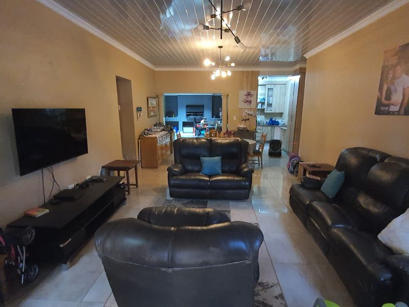 Open-plan living area featuring tiled flooring and a glossy ceiling finish, flowing into the kitchen space.