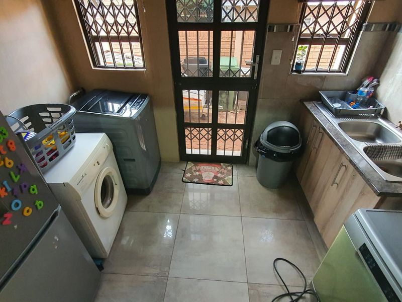 A functional laundry area featuring tiled flooring, built-in cabinetry, a double basin sink, and direct access to the exterior via a security gate.