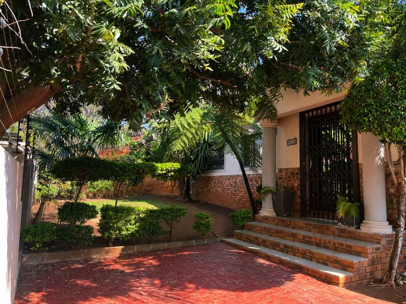 Front entrance of the townhouse featuring brick paving, a landscaped garden, and a covered porch area with decorative columns.