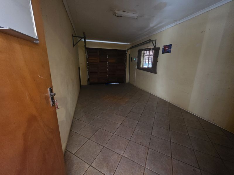 A spacious, empty garage featuring tiled flooring, a sectional garage door, and security bars on the window.
