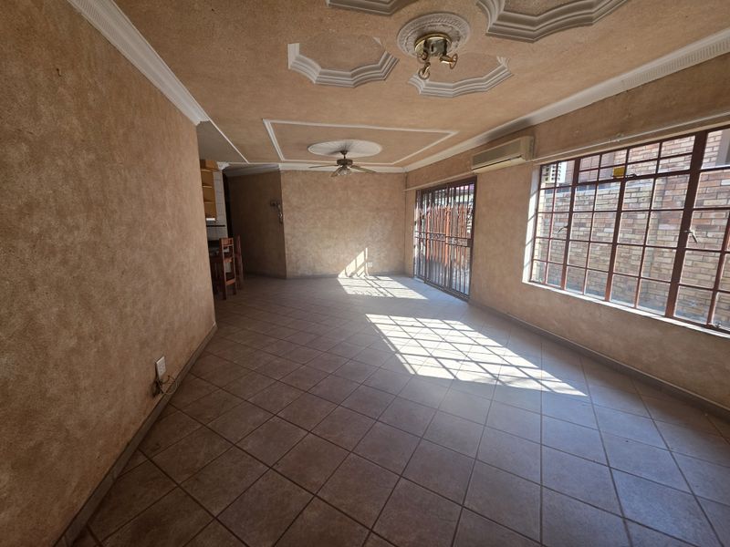 Spacious open-plan living area featuring tiled flooring, decorative ceiling roses, a ceiling fan, and a wall-mounted air conditioning unit.