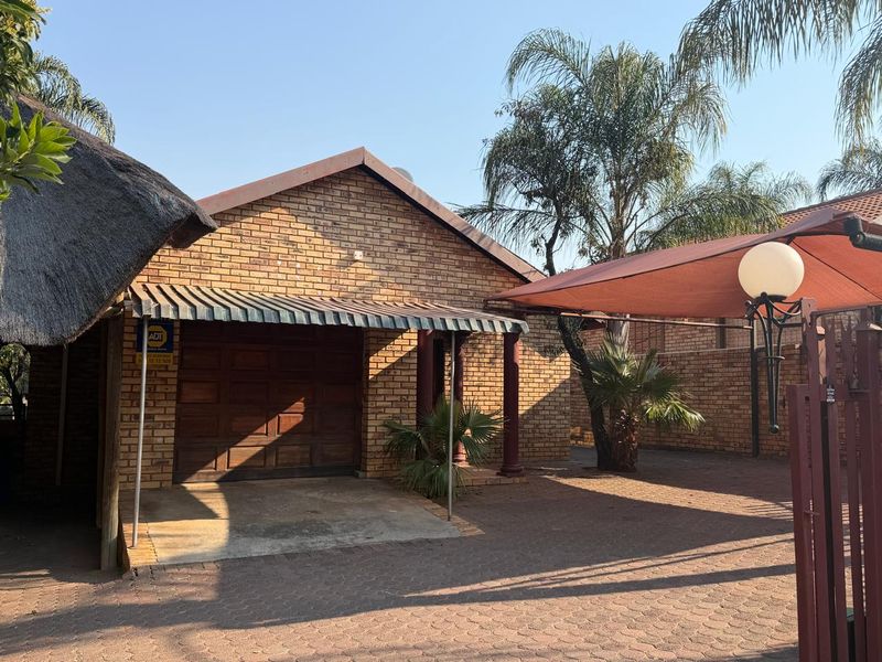 Front exterior view featuring a brick facade, single garage, paved driveway, and a shade sail structure.