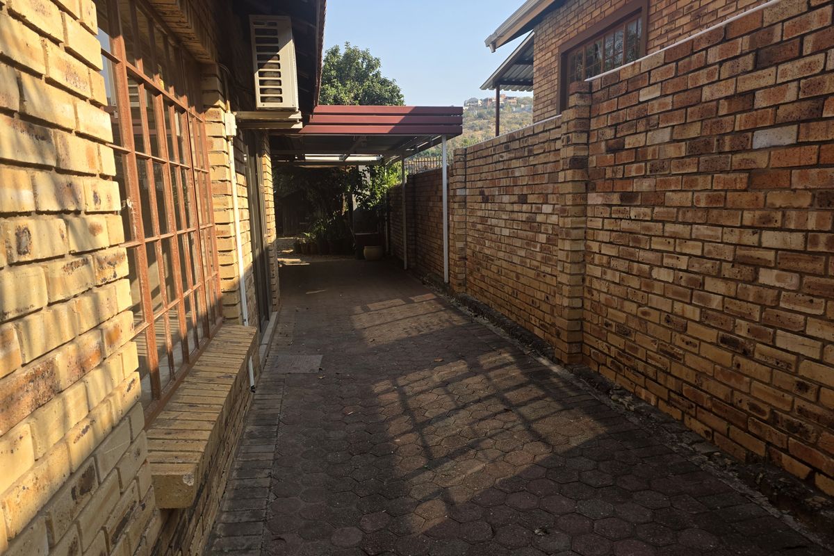 A side passage featuring face brick walls, paved flooring, and a covered carport area, providing functional outdoor access along the side of the house.