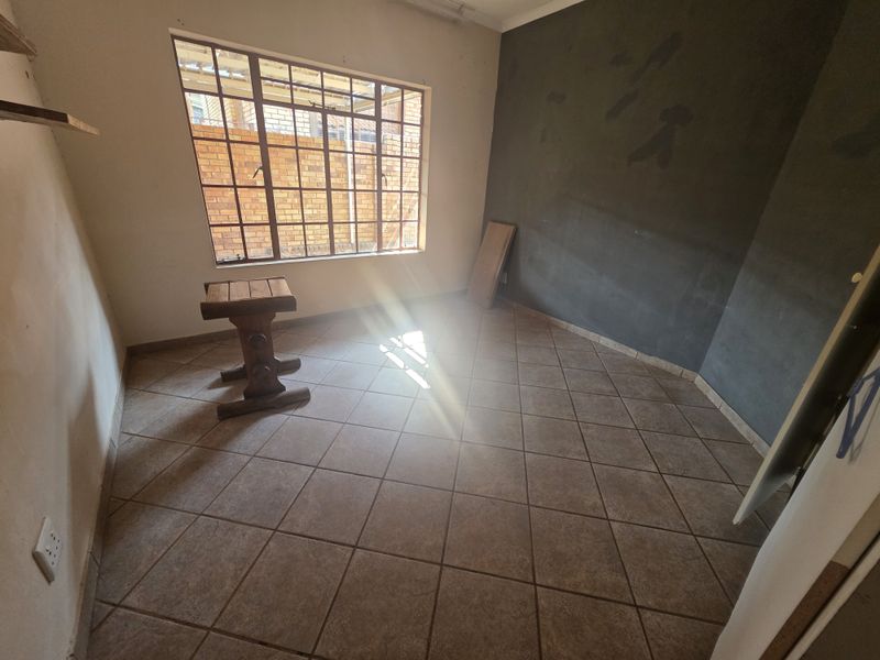 An empty bedroom featuring tiled flooring and a steel-framed window, currently requiring wall finishing and cosmetic updates.