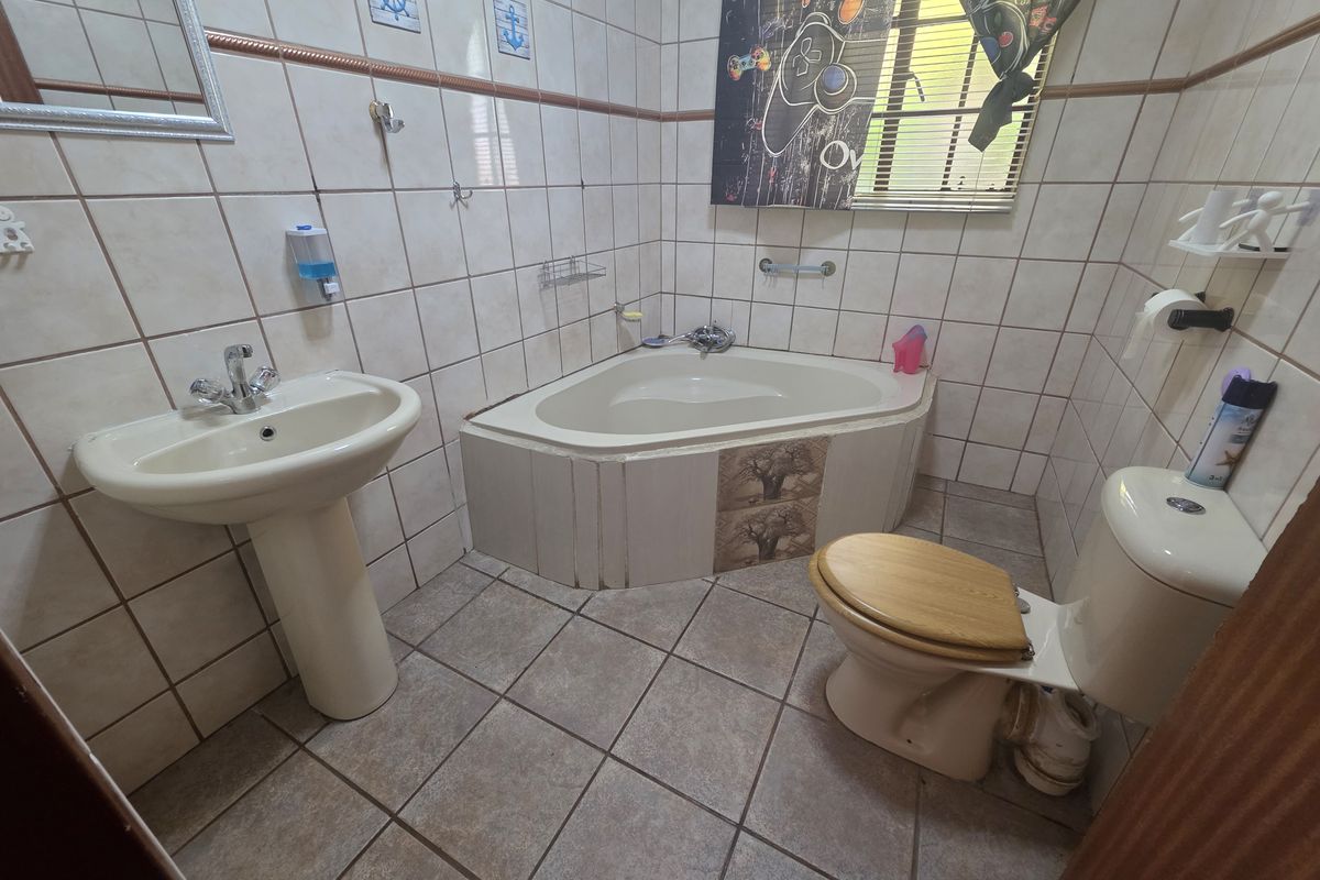 A functional bathroom featuring a corner bathtub, pedestal basin, and toilet, finished with neutral ceramic wall and floor tiles.