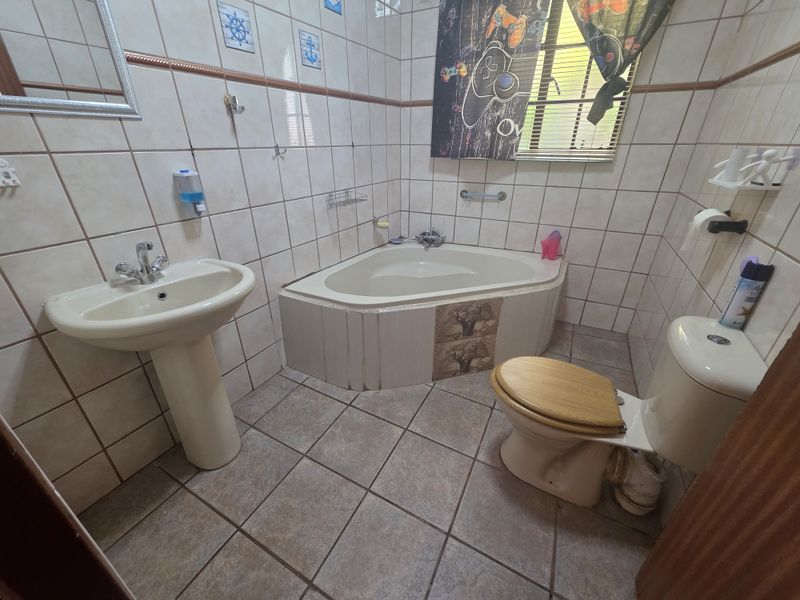 A functional bathroom featuring a corner bathtub, pedestal basin, and toilet, finished with neutral ceramic wall and floor tiles.