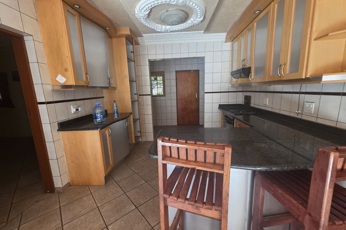 A functional kitchen featuring wooden cabinetry, granite countertops, a built-in hob with extractor fan, and tiled flooring with a decorative ceiling rose.